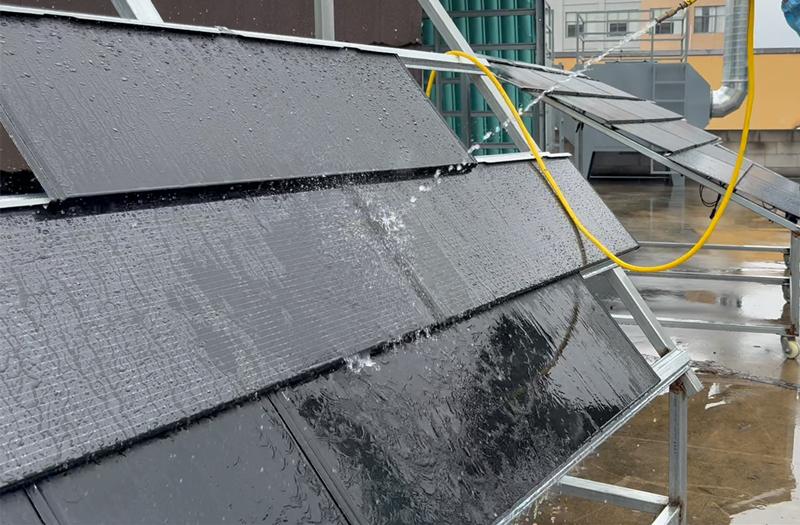 Simulation test and water spray demonstration of waterproof performance of solar photovoltaic tiles The waterproof performance test of the photovoltaic tile roof is being conducted by using a high-pressure water hose to simulate a rain shower on the solar photovoltaic tiles installed on a sloping roof.