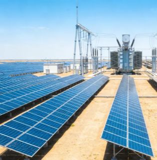 Utility-Scale Ground-Mounted Solar Farm with High-Voltage Transformer Station A real-world view of a large-scale, centralized ground-mounted solar photovoltaic power station. On a vast sandy plain, long arrays of deep blue solar panels stretch into the distance. At the far right of the array's end, a giant industrial high-voltage transformer is installed, connected to a dense network of power transmission cables and supported by a towering metal gantry structure. To the left is a white grid-connected housing, set against a clear blue sky, comprehensively showcasing the industrial scene of grid-level photovoltaic power generation and voltage boosting systems.