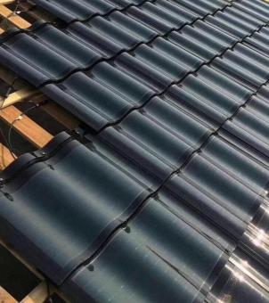 This close-up photograph deconstructs the details of modern Building Integrated Photovoltaics (BIPV) solar roof tile installation and electrical wiring. The image employs a diagonal perspective composition from lower left to upper right: the right side is largely covered with overlapping, smooth, mirror-like, and beautifully wavy dark black solar photovoltaic tiles, their surfaces reflecting bright white highlights and a deep industrial texture under the oblique sunlight. In the partially covered construction area on the left, the underlying horizontally parallel light yellow wooden shingle frame is clearly visible; in the shadows where the wooden frame connects to each layer of black tiles, thin, long black photovoltaic DC cables and series connectors are precisely concealed and extend outwards. The entire image focuses on a specific part of the construction project, showcasing the exquisite installation process that combines the building material properties of solar tiles with electrical technology from a rigorous and clear microscopic perspective.
