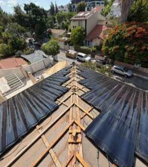 GreenMore residential rooftop construction showing the installation process and technical support for laying curved solar tiles on a wooden frame.