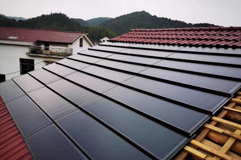 A residential BIPV solar roof installation site showcases the overlapping of black flat photovoltaic tiles and red traditional roof tiles.
