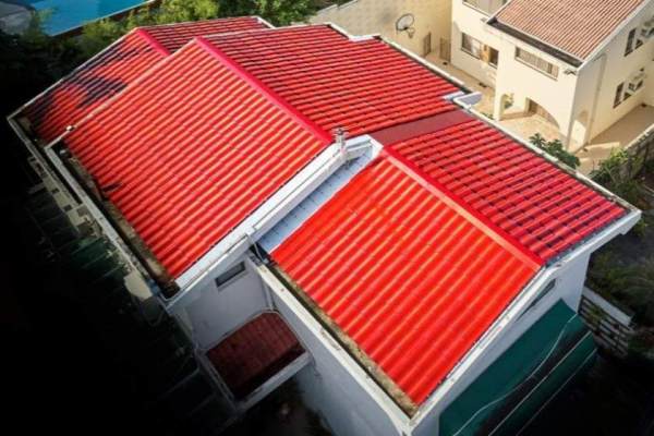 Real-life photo of a GreenMore residential building with red triple-curved arched solar tiles on its multi-sloped roof.