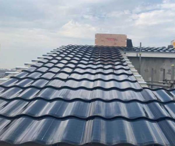 Details of the dark gray, tri-curved arched solar tiles being installed on the roof of a GreenMore building.