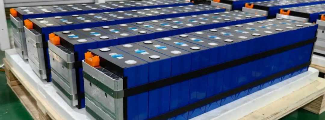 A real-life photo of square lithium iron phosphate battery modules neatly arranged on a pallet in the workshop.