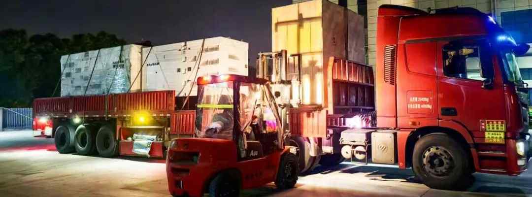 Real-life image of forklifts loading large industrial and commercial energy storage cabinets onto flatbed trucks at GreenMore factory park at night.